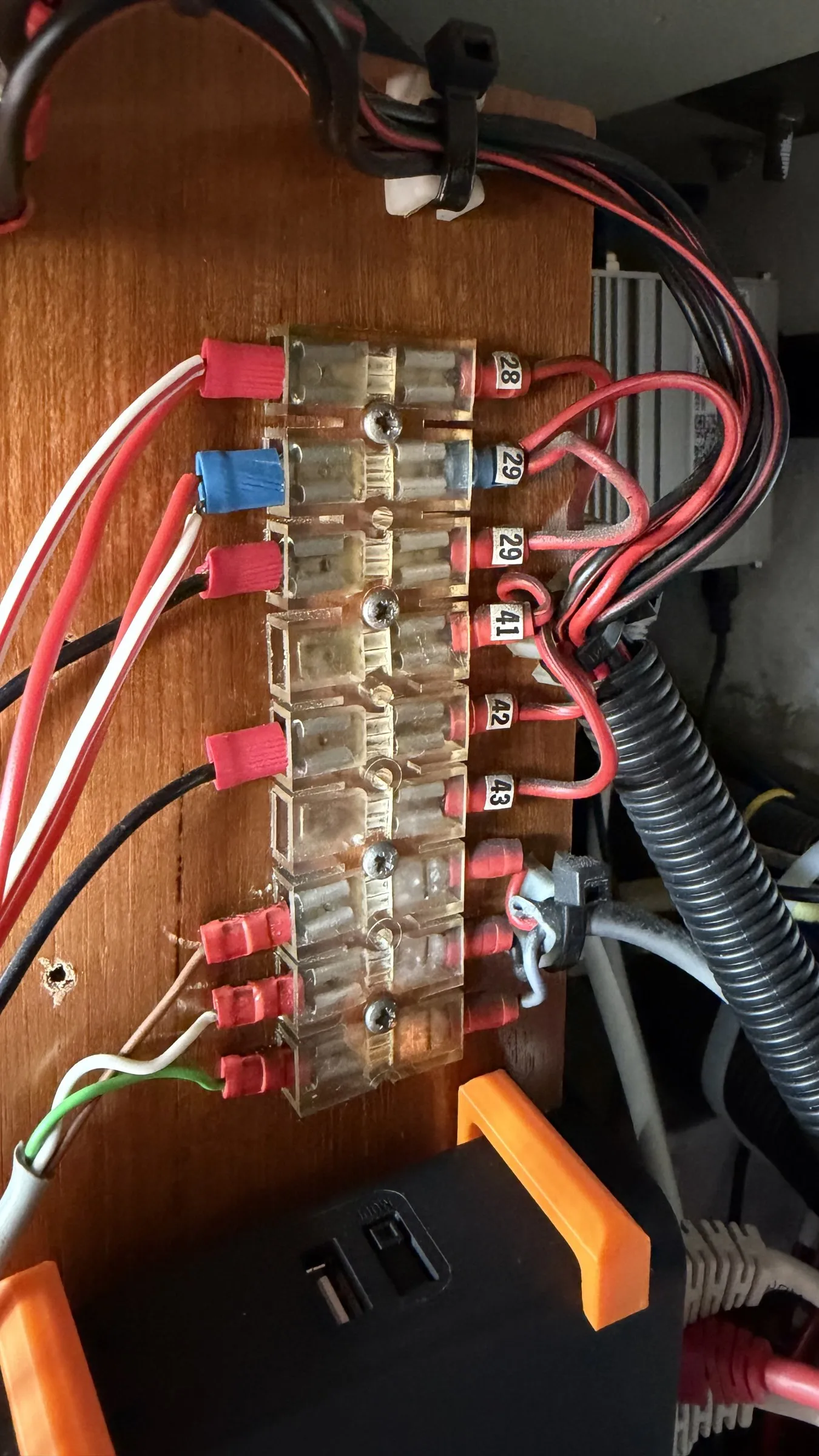 A nine-way barrier strip on a teak panel, its tabs numbered 28, 29, 29, 41, 42 and 43, with red and white wires landed on them