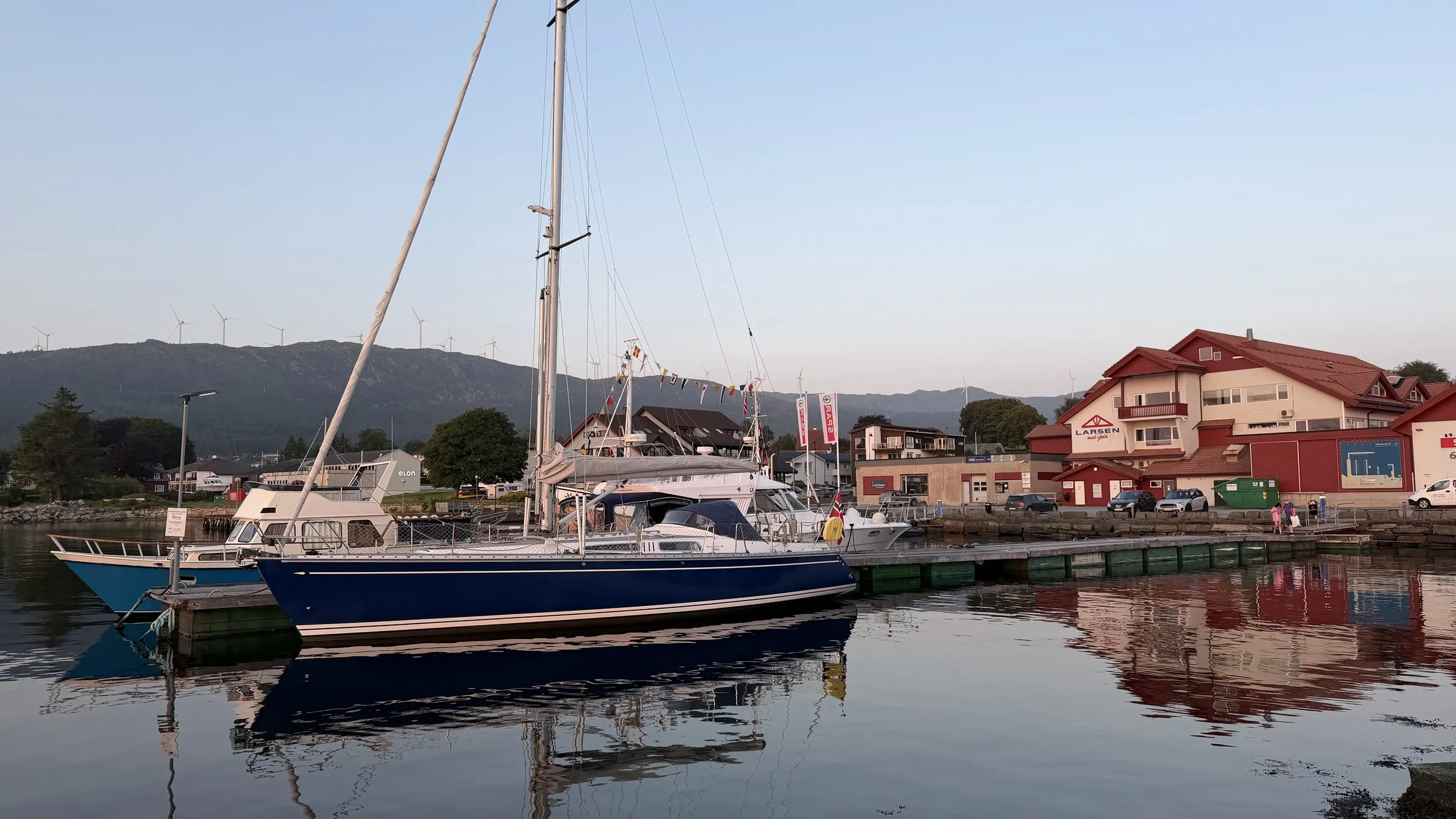 Enja lying alongside a stone quay in low evening light, wind turbines on the ridge behind