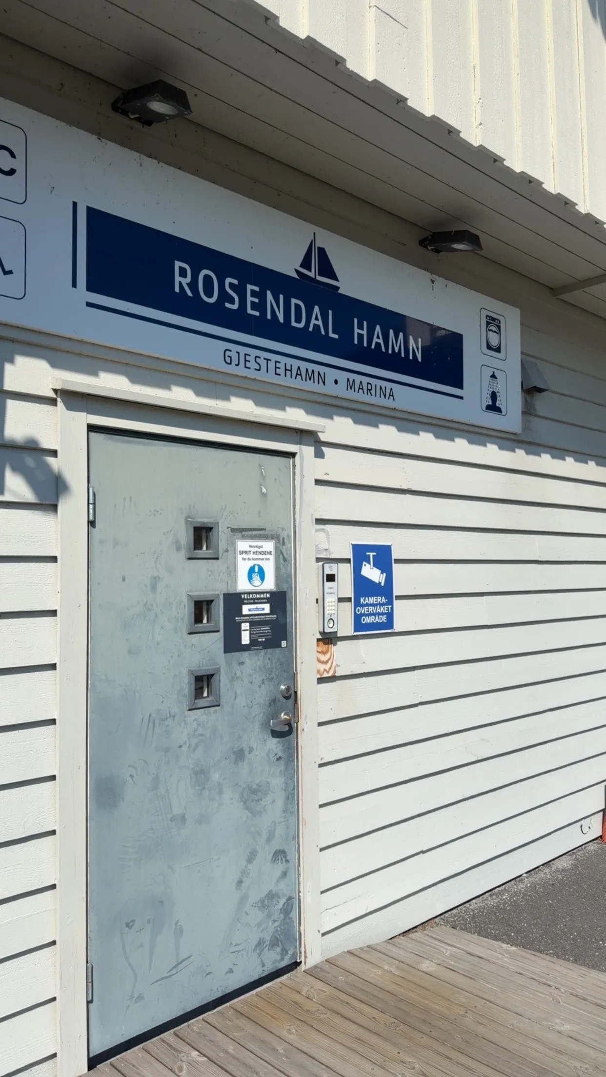 A harbour building with a blue sign reading Rosendal Hamn, Gjestehamn, Marina, in bright sunlight