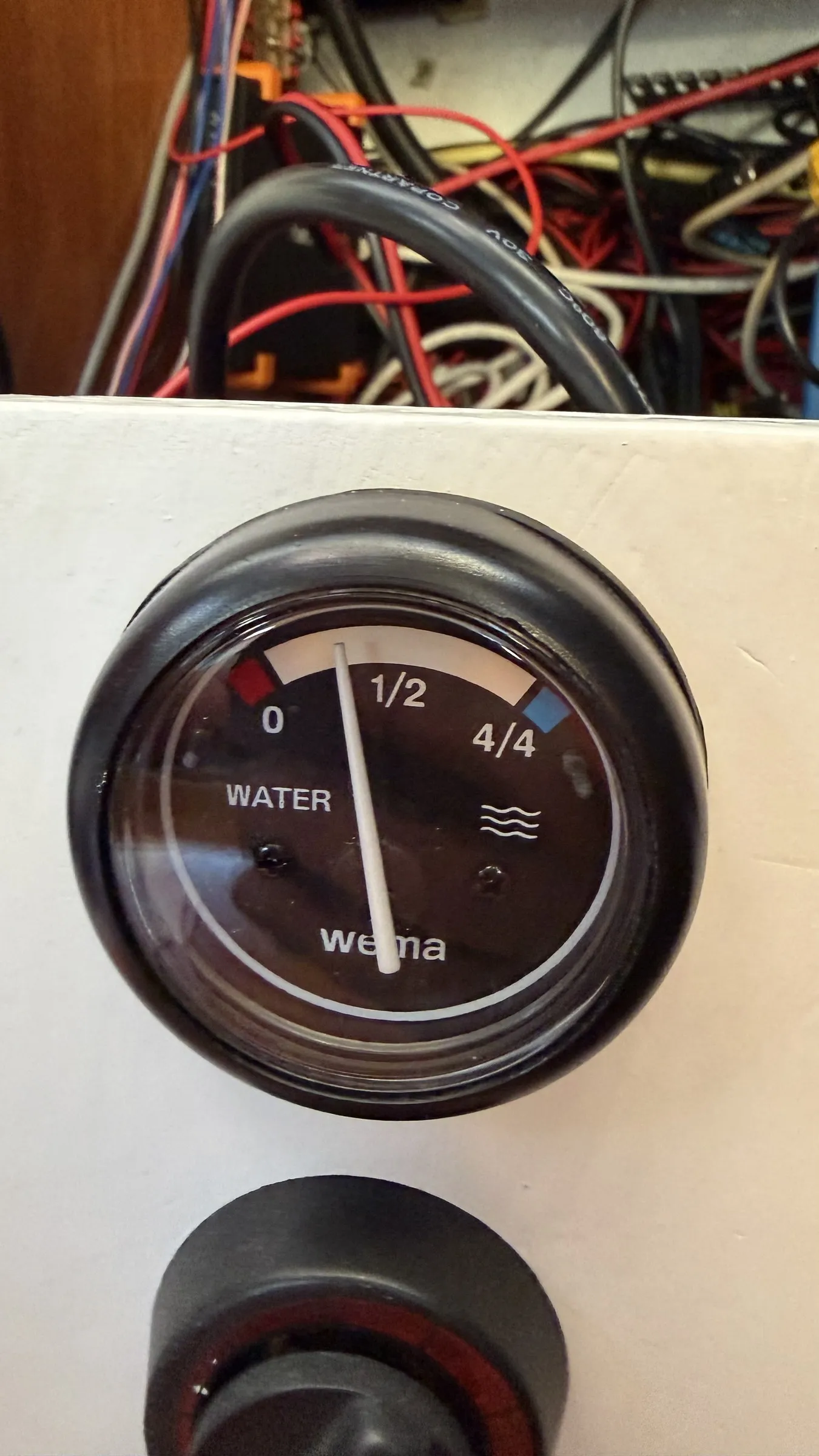 A round black WEMA water tank gauge in a white panel, scaled 0 to 4/4, its needle resting mid-dial